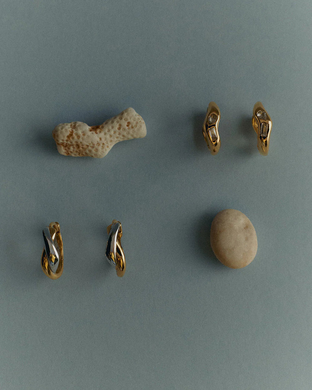 Gold earrings with a piece of coral and a stone on a gray background